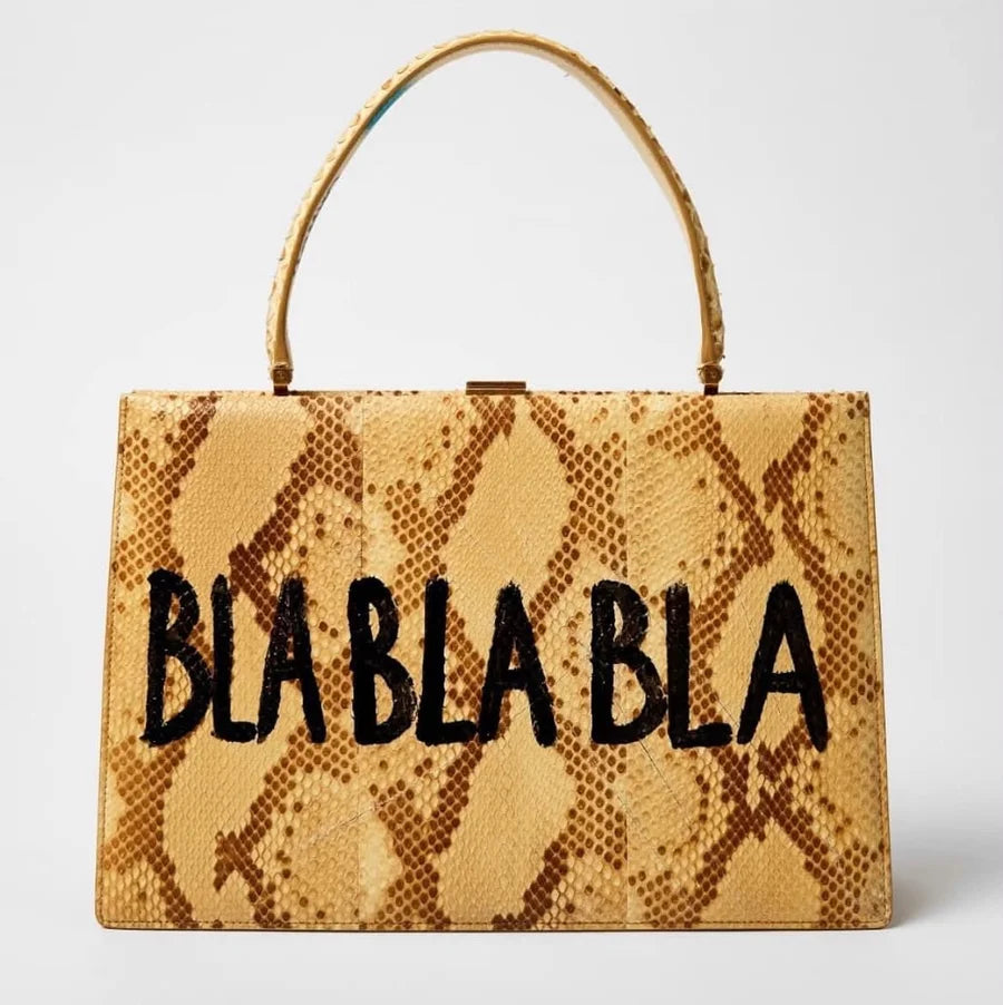 A golden patterned handbag with black BLA BLA BLA lettering
